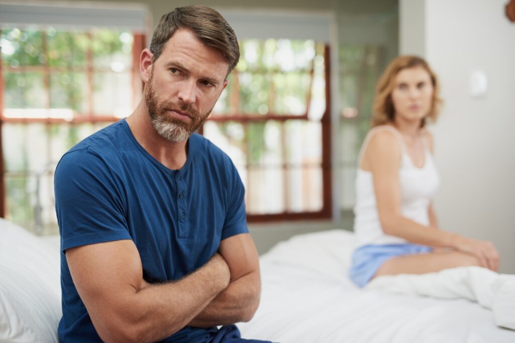 Homem e mulher sentados na cama - representação de impactos da atrofia vaginal. 