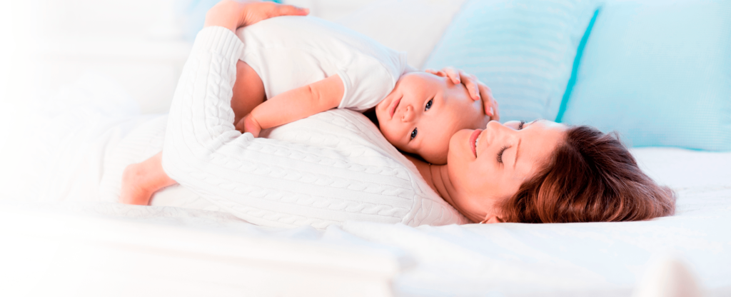 Mãe deitada na cama segurando seu filho bebê no colo.
