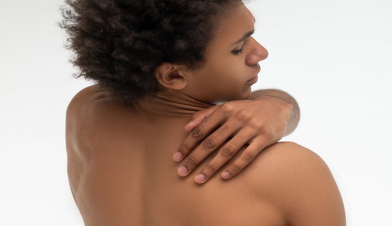 Homem pele negra coçando as costas em sinal de sintoma da dermatite atópica