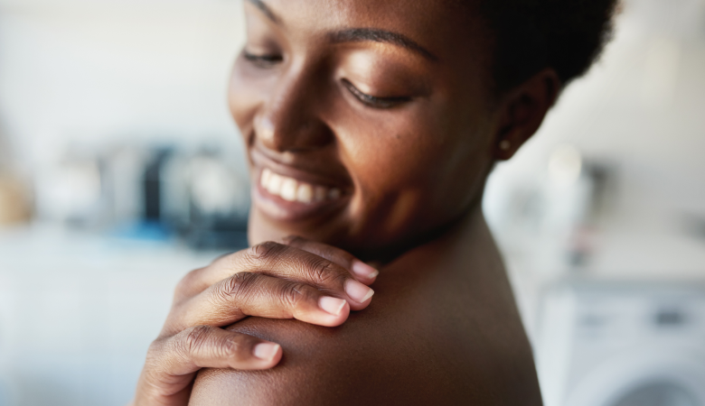 Mulher com a mão no ombro, foco no corpo, em sinal de seus cuidados com a pele do corpo.