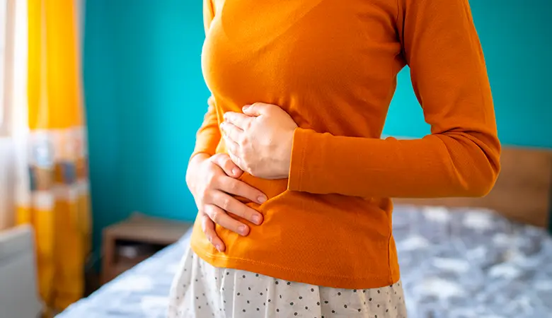 Mulher com dor abdominal decorrente de prisão de ventre, pensando em administrar um laxante.