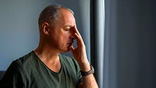 Homem com crises de sinusite, com a mão na testa em sinal de dor.