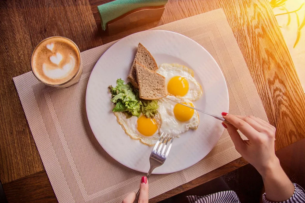 ovo frito com a gema mole, junto a pedaços de pão integral, alface e um copo de café
