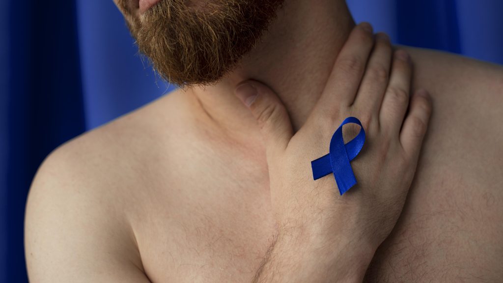Homem de barba com a mão apoiada no pescoço exibindo um laço de fita azul em apoio ao Novembro Azul e às pessoas que enfrentam o câncer de próstata