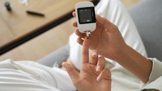 mãos de uma mulher com diabetes utilizando um aparelho para checar seu nível de glicose
