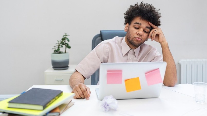 homem com atitude entediada em um escritório, com dificuldade para se concentrar, com um notebook aberto em sua frente, representando os prejuízos ao trabalho provocados pelo TDAH